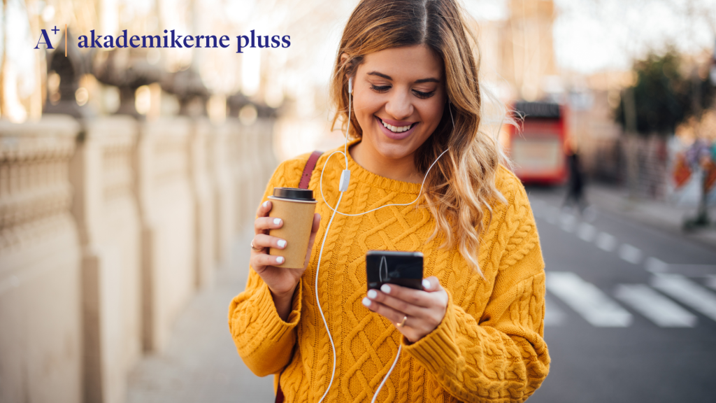 Illustrasjonsfoto for medlemsapp: Ung kvinne ser ned på mobiltelefonen mens hun går langs en gate.